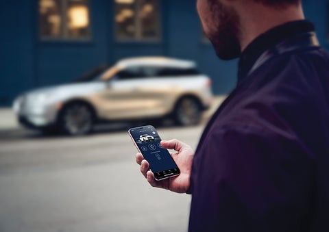 A person is shown interacting with a smartphone to connect to a Lincoln vehicle across the street. | Thornhill Lincoln in Chapmanville WV